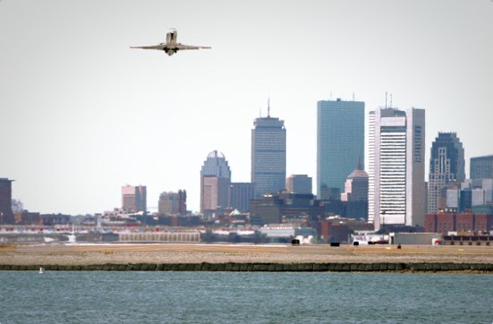 A plane flying over the water with a city in the background.